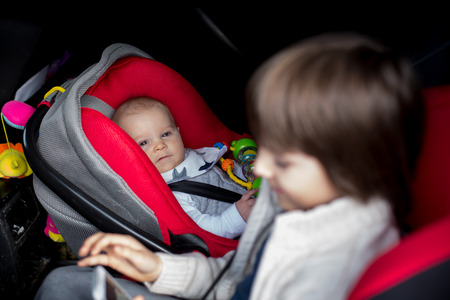 Little baby boy and his older brother, traveling in car seats, going on a holiday, preschool boy playing with mobile phoneの写真素材