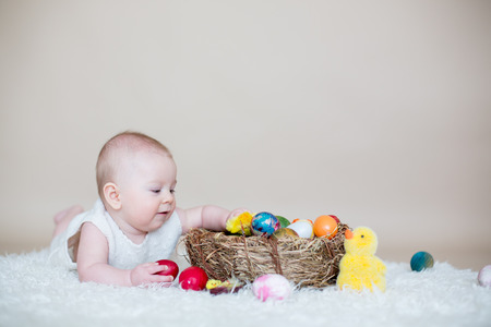 Cute little toddler baby boy, playing with colorful easter eggs and little decorative ducks, isolated shot, beige backgroundの写真素材