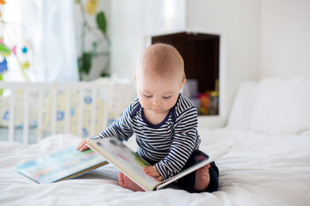 Portrait of a cute smiling infant baby boy reading a book. Happy childhood concept.の写真素材