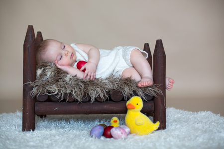 Cute little toddler baby boy, sleeping with colorful easter eggs and little decorative ducks, isolated shot, beige backgroundの写真素材