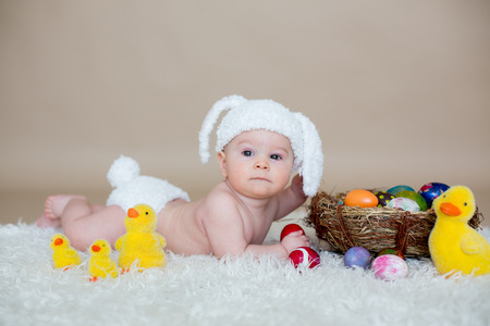 Cute little toddler baby boy, playing with colorful easter eggs and little decorative ducks,...