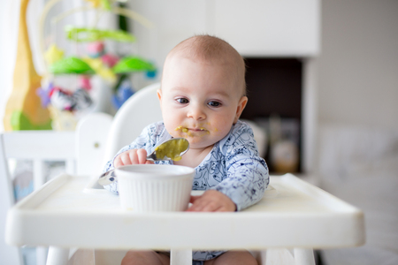 Cute little baby boy, eating mashed vegetables for lunch, mom feeding him, sweet toddler boy, smilingの写真素材