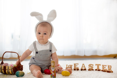 Cute little toddler child, baby boy, in sunny living room playing with  Easter chocolate bunny and colorful Easter eggsの写真素材