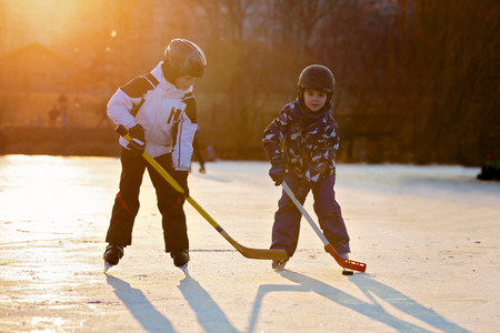 Children, boys, friends and brothers playing hockey and skating in the park on frozen lake, wintertime on sunsetの写真素材