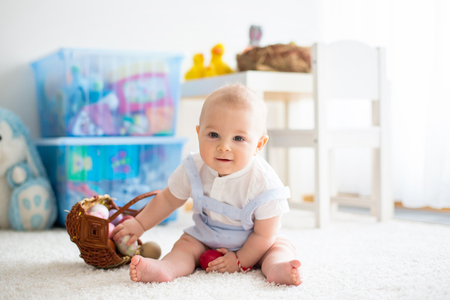 Cute little toddler child, baby boy, in sunny living room playing with  Easter chocolate bunny and colorful Easter eggsの写真素材