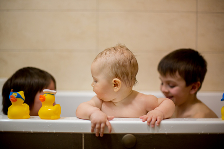 Little baby boy, playing with rubber ducks in bathtube with his siblingsの写真素材