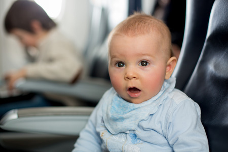 Cute baby boy, playing with toys on board of aircraft, traveling on vacation with parents and...