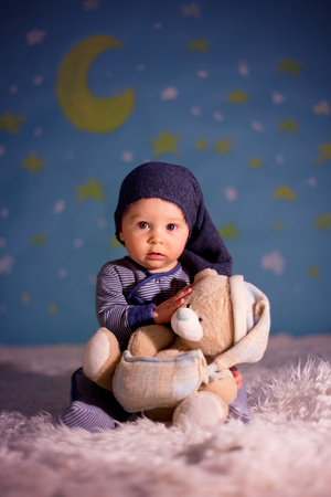 Little child, baby  boy with cute teddy bear and moon on a blue star and moon background, sleeping, playingの写真素材