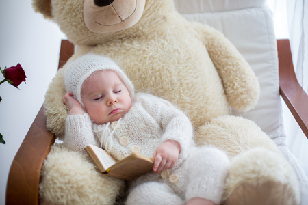 Sweet little baby boy, sleeping with huge teddy bear in big armchair, littlr table with vase with roses flowers next to himの写真素材