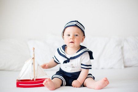 Cute baby boy, dressed in sailor clothes, playing with wooden boatの写真素材