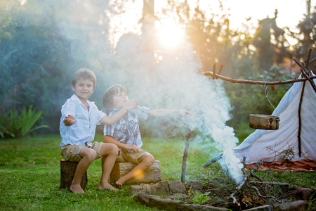 Two sweet children, boy brothers, camping outside summertime on sunset, eating potatoesの写真素材