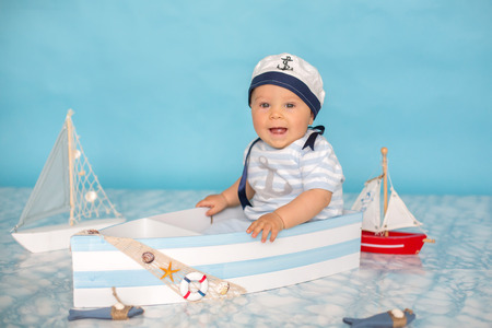 Cute toddler baby boy in wooden boat, playing with fishes, starfish and binoculars as sailman, studio indoors shotの写真素材