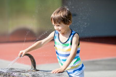 Sweet child, boy, splashing water from a fountain, happiness summertimeの写真素材