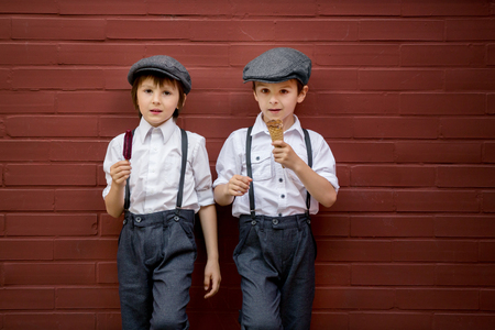 Little preschool boys, cute children, dressed in vintage style clothes, eating ice cream, urban sceneの写真素材