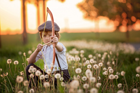Portrait of child playing with bow and arrows, archery shoots a bow at the target on sunsetの写真素材