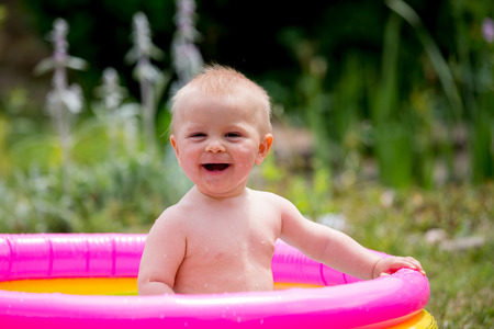 Cute little child, toddler boy, playing in small baby pool in backyard, having fun