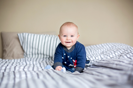 Cute little baby boy, playing at home in bed with lots of colorful toys for babies and toddlers