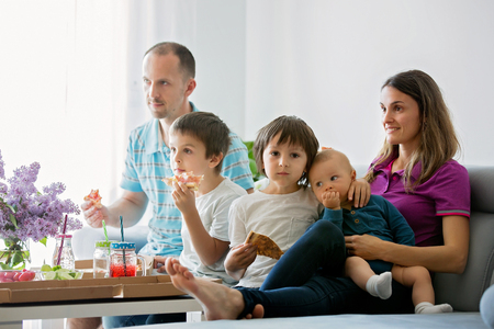 Beautiful young family with three children, eating pizza at home and watching TV on a sundayの写真素材