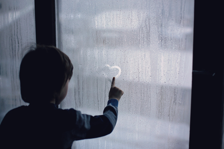 Little boy, leaving finger prints and drawing hearts on a window at homeの写真素材