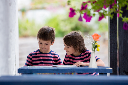 Children reading map and planning roda trip, sitting on a small blue table on the hotel porch, summertimeの写真素材