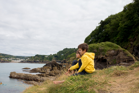Children, enjoying quiet cloudy day on the ocean shore on the cliff, rocky beach in Englandの写真素材