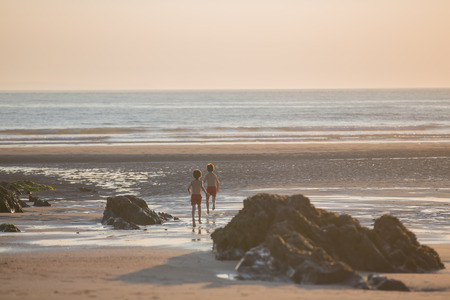 Sailor baby boy, cute child, playing on the beach with wooden boat, fishes and fishing rod on sunset by the oceanの写真素材