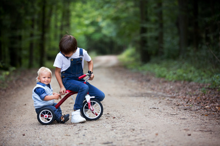 Cute toddler child and his older brothers, boys, siblings, playing with tricycle in park, having funの写真素材