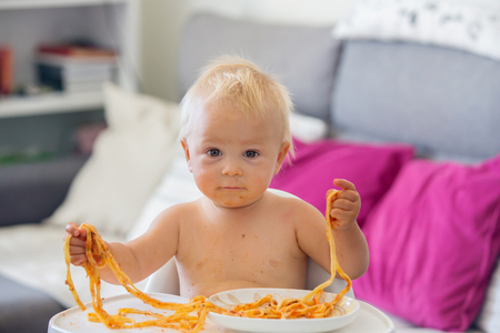Adorable little baby one year old eating pasta indoor. Funny toddler child with spaghetti. Cute kid and healthy food.の写真素材