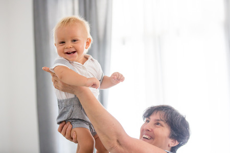 Grandmother holding happy baby at home, in living room