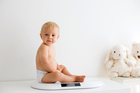 Pediatrician examining baby boychecking his weight in sunny roomの写真素材