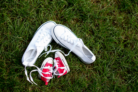 Red baby toddlers sneakers and white woman sneakers on the grass, lased togetherの写真素材