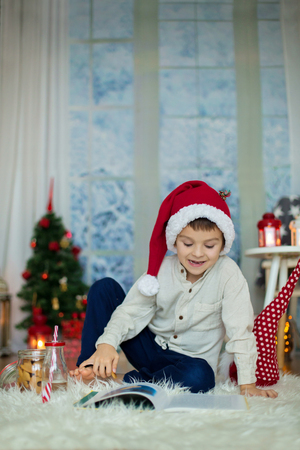 Cute preschool child, boy, reading a book and eating cookies at home, while snowing outdoorsの写真素材