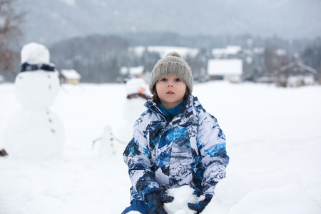 Family with children, building snowman in the park in little village in Austria, beuatiful landscape sceneryの写真素材