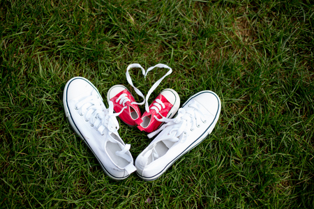 Red baby toddlers sneakers and white woman sneakers on the grass, lased togetherの写真素材