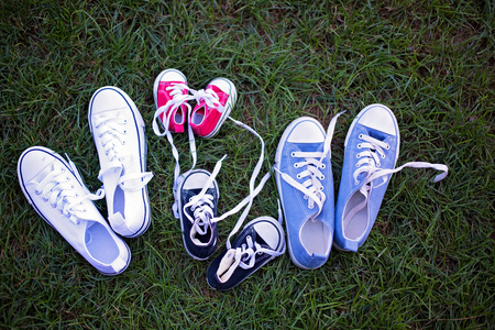Four different colors pair of sneakers, shoes for the whole family lying on the grassの写真素材