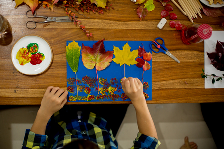 Children, applying leaves using glue, scissors, and paint, while doing arts and crafts in school, autumntimeの写真素材