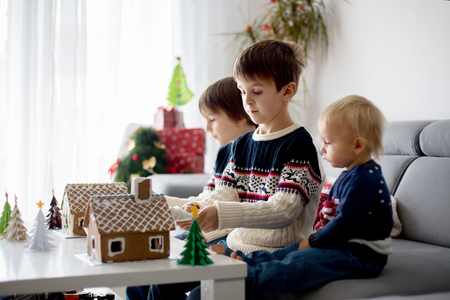 Three sweet boys, brothers, making gingerbread cookies house, decorating at home in front of the Christmas tree, child playing and enjoying, Christmas conceptの写真素材