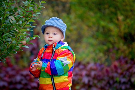 Sweet funny child with rainboy coat and multicolored umbrella jumping on puddles iand playing outdoors after rainの写真素材