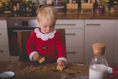Sweet toddler child, boy, helping mommy preparing Christmas cookies at home in kitchenの写真素材