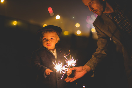 Waist up portrait of happy family celebrating New Year together and lighting sparklers outdoors in gardenの写真素材