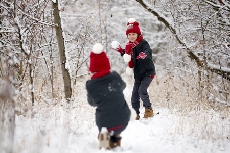 Cute little toddler boy and his older brothers, playing outdoors with snow on a winter day, snowingの写真素材