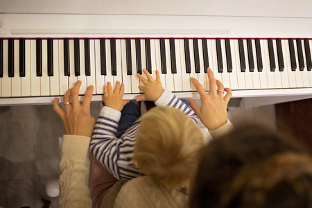 Sweet positive toddler child and mother playing piano. Early music education for little kids, children at home learning music instrumentsの写真素材