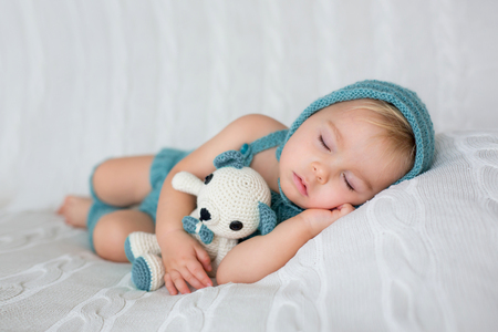 Sweet toddler boy, sleeping with teddy bear toy, cute knitted outfit, isolatedの写真素材