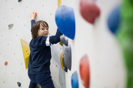 Sweet little preschool boy, climbing wall indoors, having fun, active children