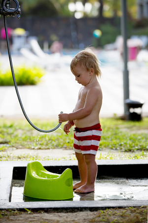 Sweet toddler boy, washing his potty on outdoor sink and showers on the beachの写真素材