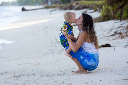 Mom and toddler boy, happily hugging on the ocean shore, relaxing and enjoying the sunの写真素材