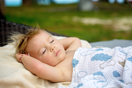 Cute blond toddler boy, sleeping on a big round beach chair on the deck of pool next to the beach on tropical island of Mauritiusの写真素材