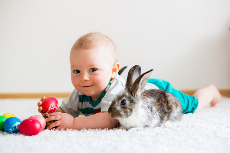 Little toddler child, baby boy, playing with bunnies and easter eggs at home, colorful hand drawings on the eggs