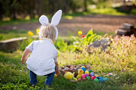 Sweet toddler boy with bunny ears, egg hunting for Easter, child and Easter day traditions. Kids and holidaysの写真素材