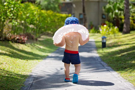 Child with suntan lotion shaped as smile on his back, going at the beach with toys and inflatable ring. Concept for sun protection and skin care for childrenの写真素材